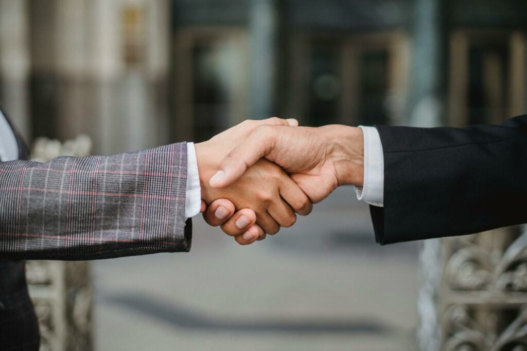 Gros plan de deux personnes se serrant la main. L'une porte un costume à carreaux, l'autre un costume noir, symbolisant un accord commercial ou un partenariat, sur un arrière-plan flou et professionnel.